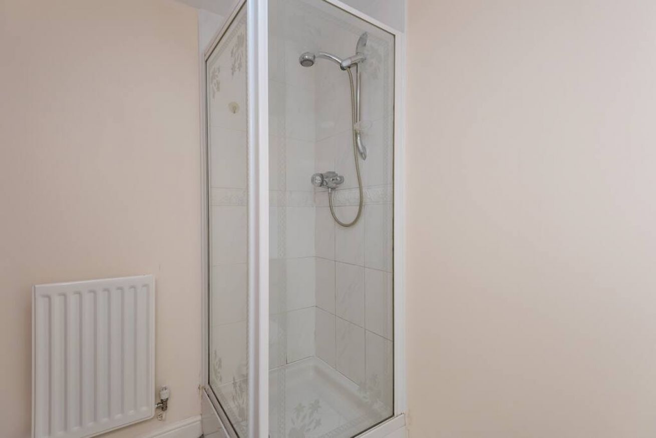Une douche fermée par des parois en verre, dotée d’un pommeau de douche à main et d’un robinet mural.