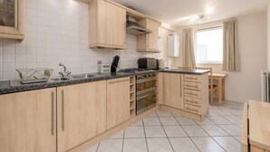 A modern kitchen with light wood cabinets, a granite countertop, stainless steel appliances, and a window with curtains. - Old Town Flat with Parking near Royal Mile (Edinburgh)