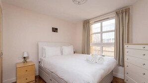 A bedroom with a large bed, a nightstand with a lamp, a dresser, and a window with curtains. - Old Town Flat with Parking near Royal Mile (Edinburgh)