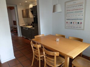 Ein Essbereich mit Holztisch und -stühlen, im Hintergrund eine Küche und ein Poster an der Wand.