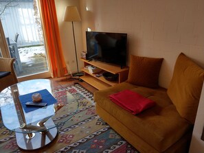 Ein Wohnzimmer mit einer Couch, einem Glastisch, einem Fernseher und einem Teppich mit Muster.