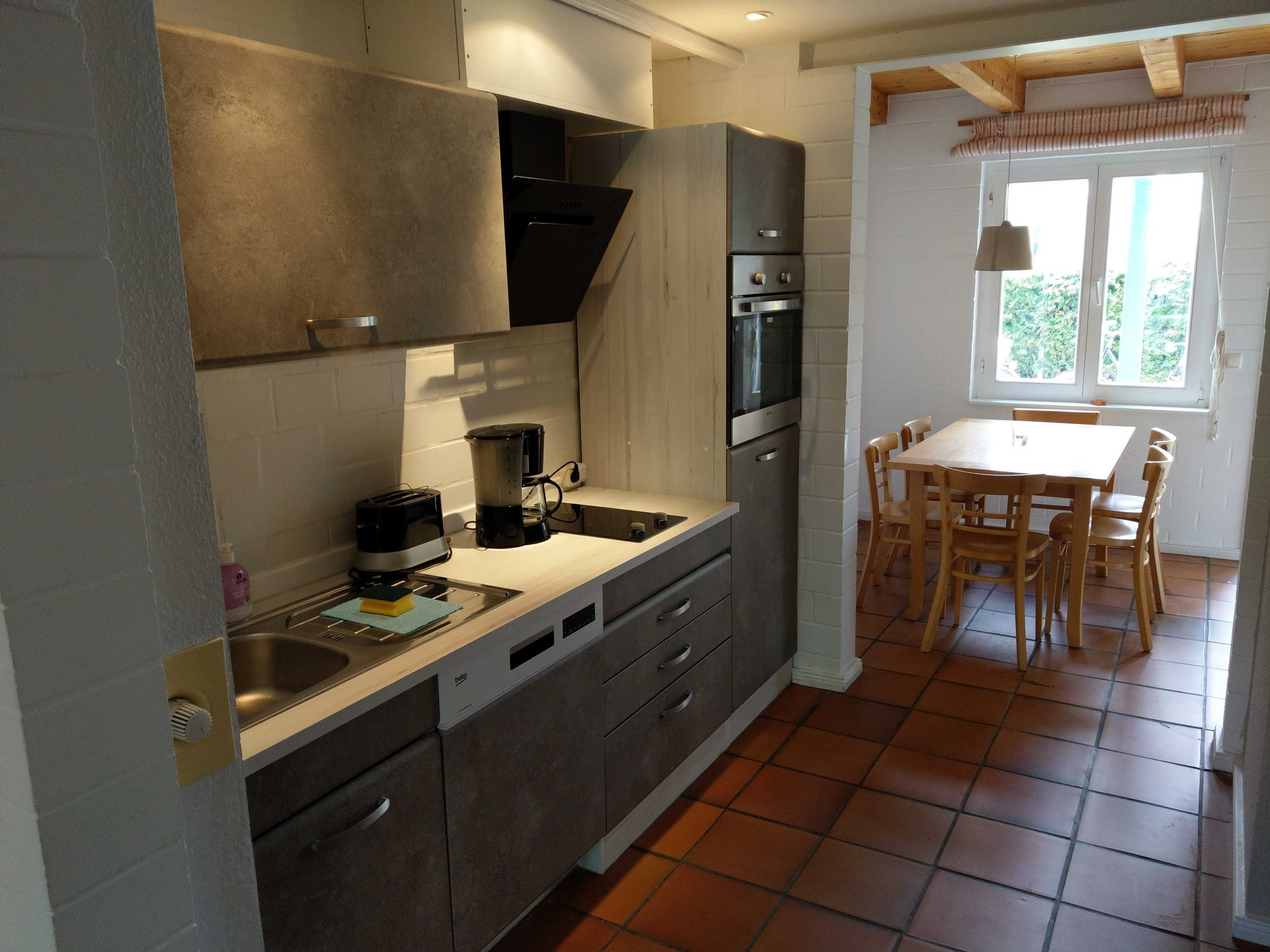 Cozinha compacta com eletrodomésticos modernos, área de jantar com mesa e cadeiras, e uma janela que oferece luz natural.