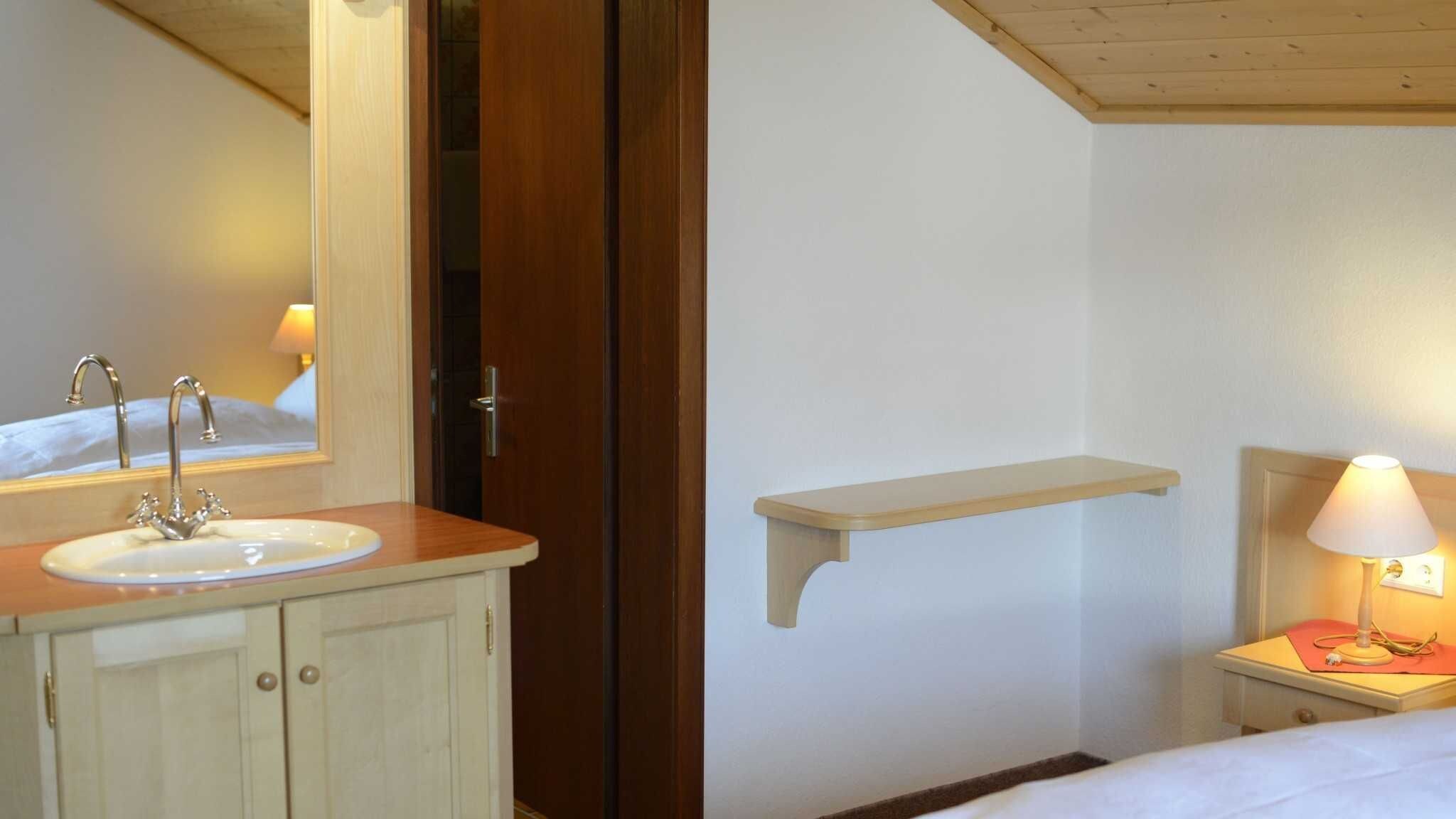 A bathroom with a sink, mirror, and a bedside table with a lamp.