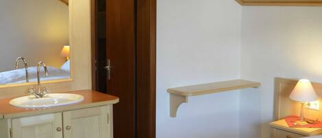 A bathroom with a sink, mirror, and a bedside table with a lamp.