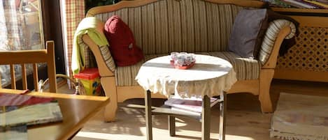 A cozy room with a wooden bench, a small round table with a lace tablecloth, and a striped sofa with a red blanket and a pillow.