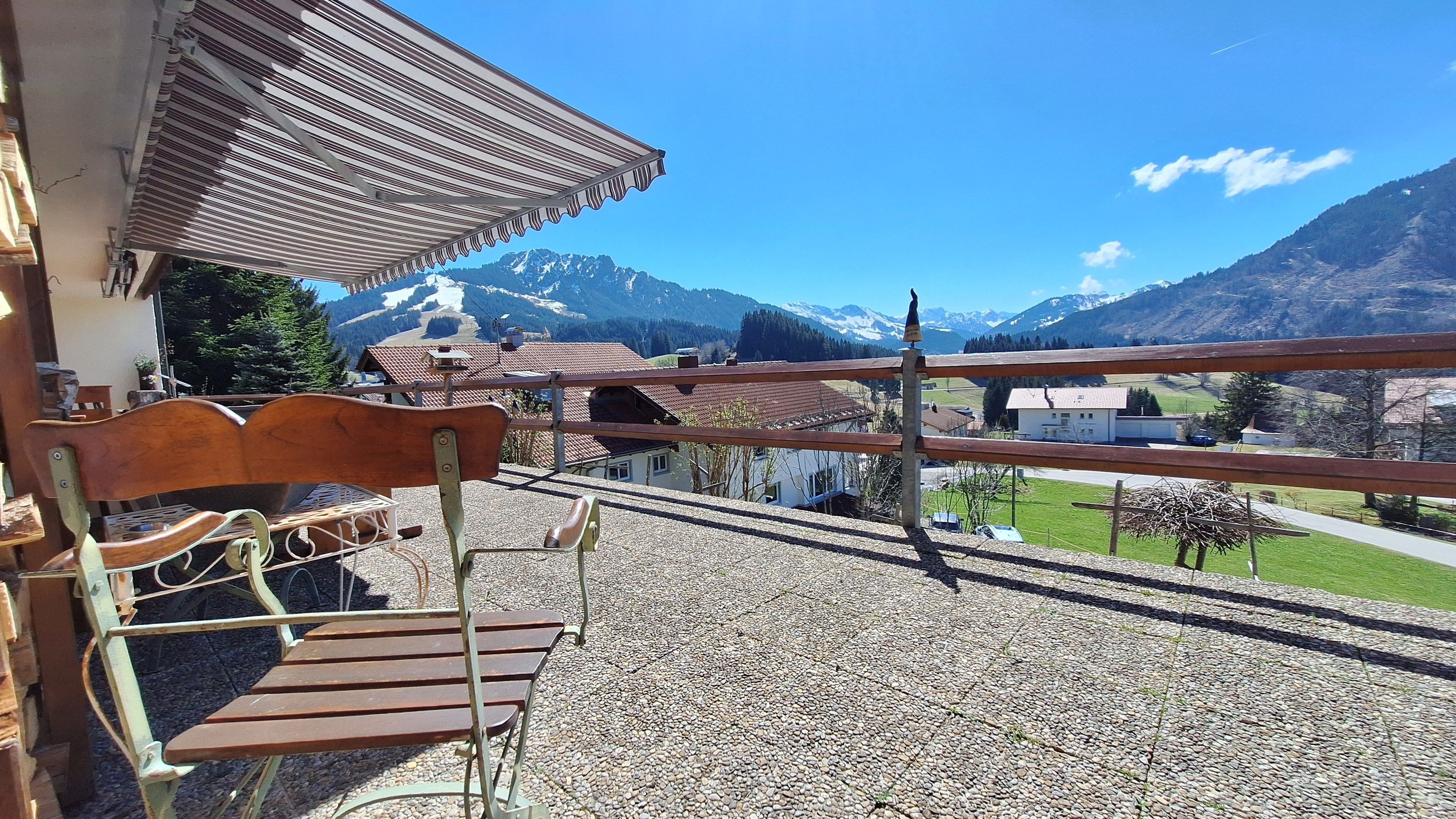 Ein Balkon mit einer hölzernen Bank, einem Metallgeländer und Blick auf eine Berglandschaft.