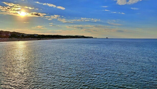 Un paysage côtier avec un ciel dégagé, une mer calme et des bâtiments situés au loin.