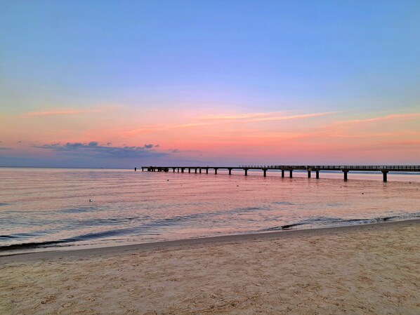 A beach with a pier extending into calm waters, under a clear sky.