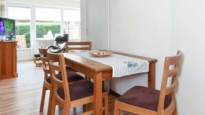 Un coin repas avec une table et des chaises en bois, un luminaire suspendu et un téléviseur en arrière-plan.