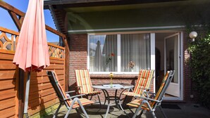 Une terrasse avec une table et quatre chaises à rayures, une clôture en bois et une porte-fenêtre coulissante.