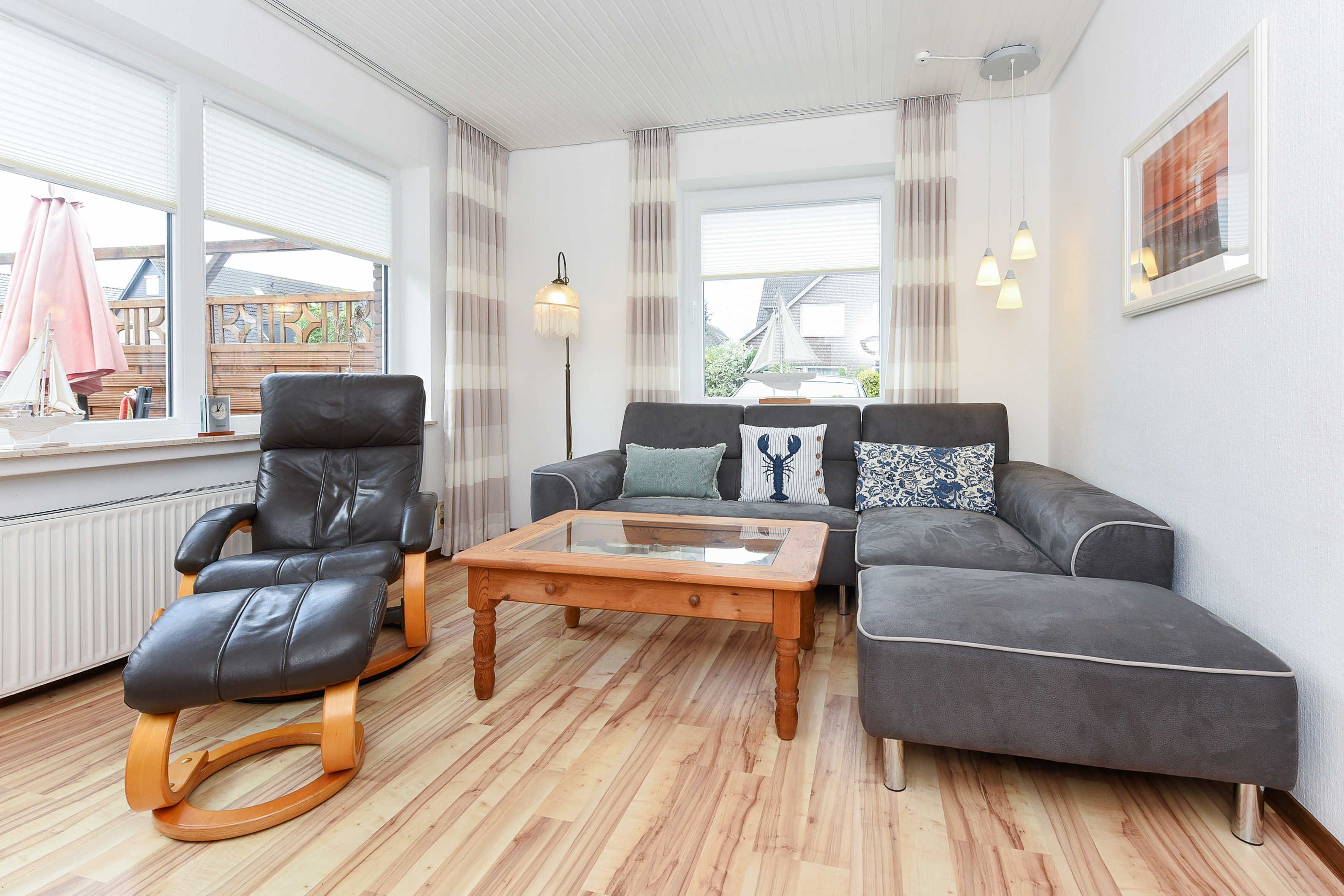 Ein Wohnzimmer mit Ledersessel, Glastisch und grauem Sofa mit gemusterten Kissen.