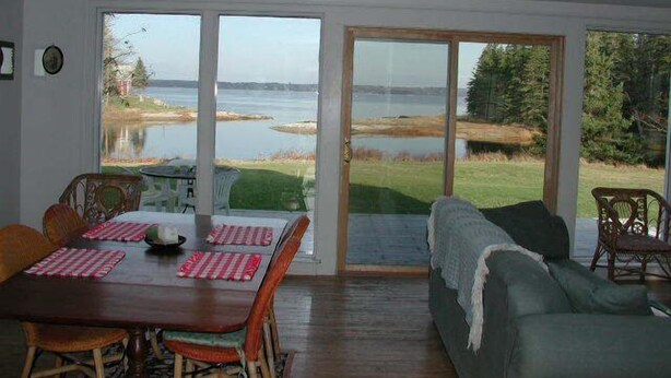 Un espace repas comprenant une table et des chaises, un canapé et de grandes portes-fenêtres coulissantes donnant sur une vue sur un lac et une forêt.