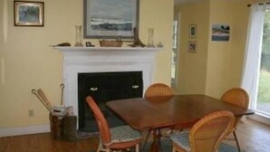 Une salle à manger avec une table en bois et des chaises en osier, une cheminée et des tableaux encadrés accrochés au mur.