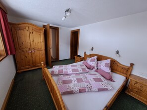 Quarto com cama de madeira, mesa de cabeceira, guarda-roupa e porta para outro cômodo.