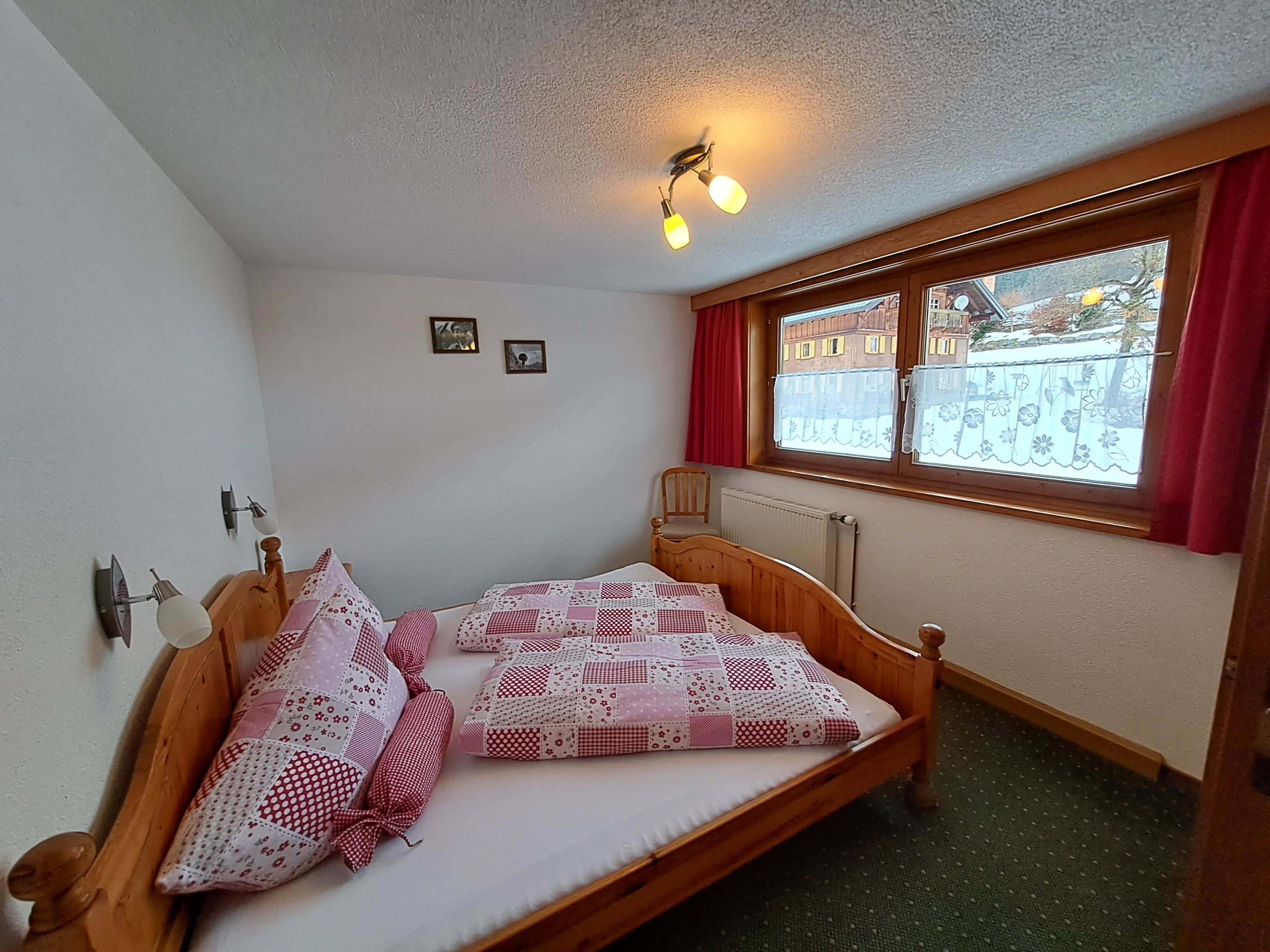 Una habitación pequeña y acogedora con una cama individual, una ventana con cortinas, un radiador y una lámpara en el techo.