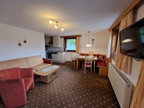 Ein kompakter Wohnbereich mit Küchenzeile, Essbereich, Sofa und an der Wand montiertem Fernseher.