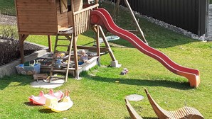 Una casita de juegos de madera con un tobogán, una mesa de picnic y un pequeño jardín.