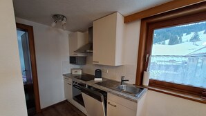 Cocina pequeña con armarios blancos, microondas integrado, tostadora, lavamanos y ventana con vistas a un paisaje nevado.