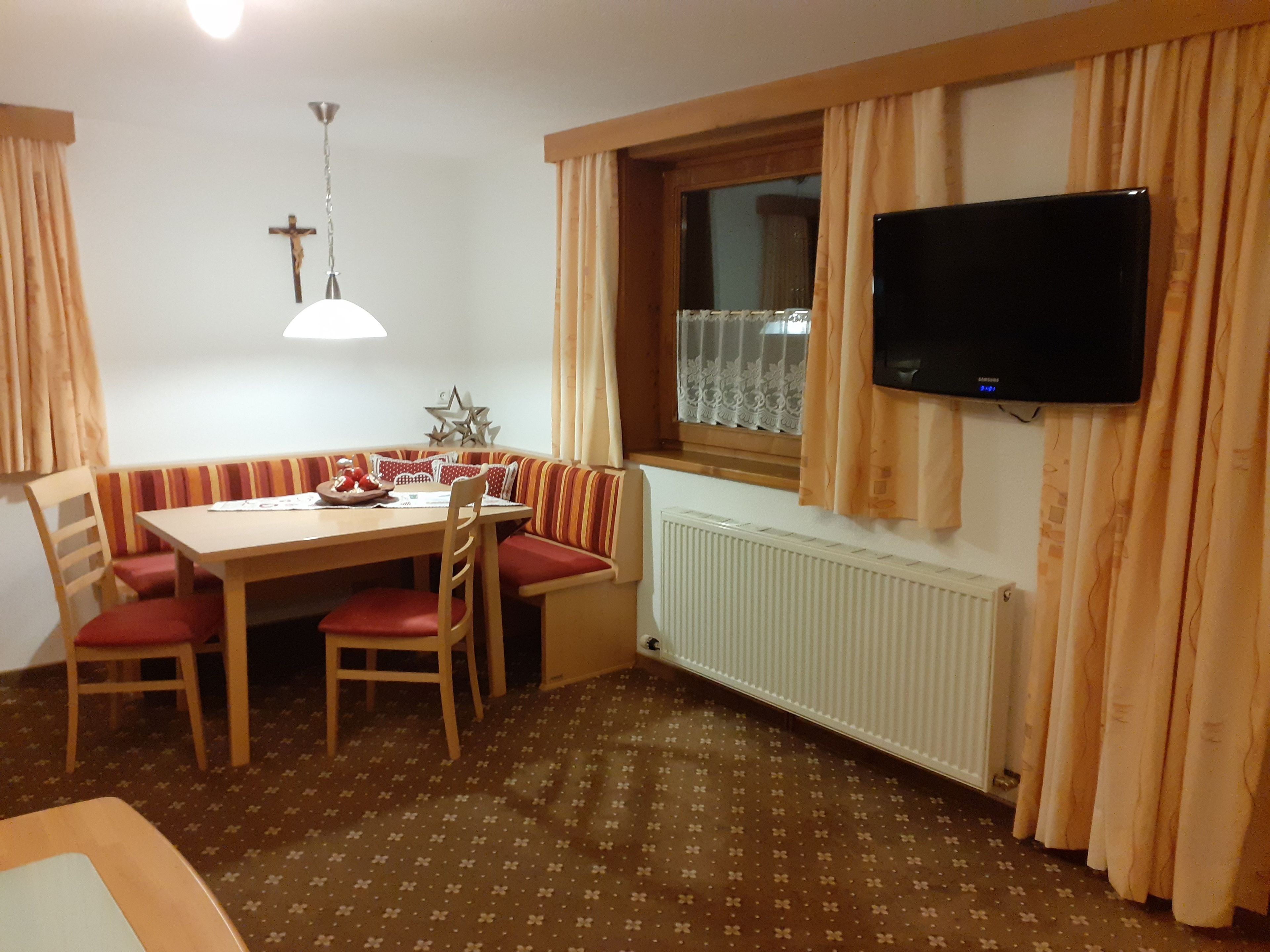 A dining area with a table, chairs, and a television mounted on the wall.