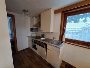 Uma cozinha compacta com armários brancos, micro-ondas embutido, torradeira, pia e janela com vista para uma paisagem nevada.