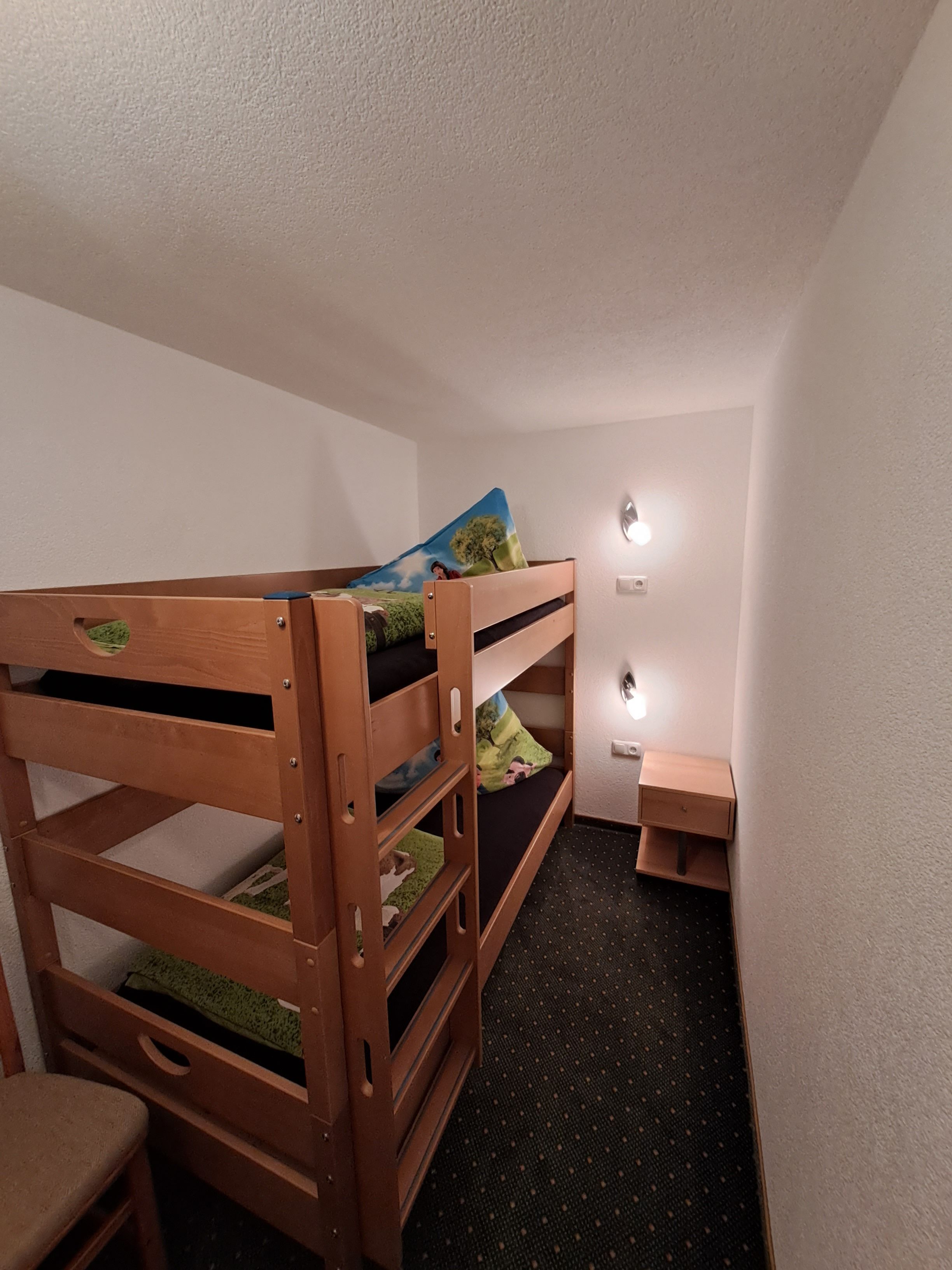A bunk bed with a green mat, a small desk, and a nightstand.