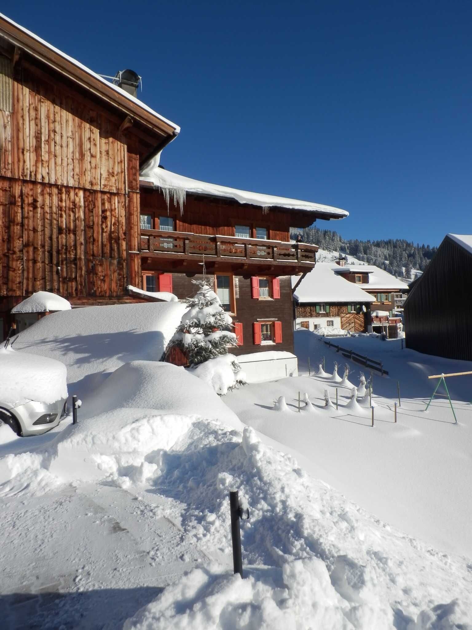 Ein hölzernes Gebäude mit verschneitem Dach, einem kleinen Baum und einem Auto mit Schneedecke.