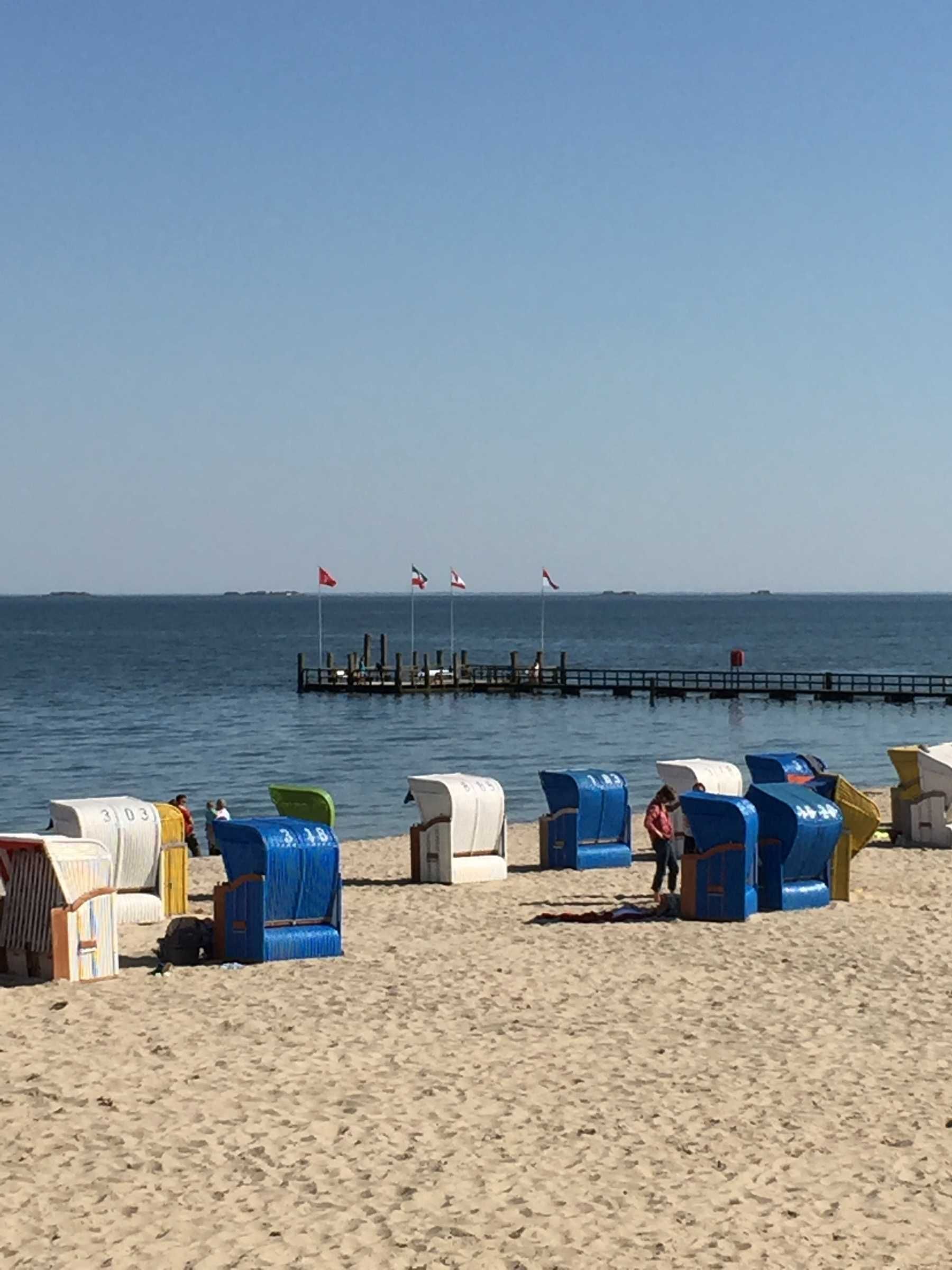 Een strand met strandhutten en een pier op de achtergrond.