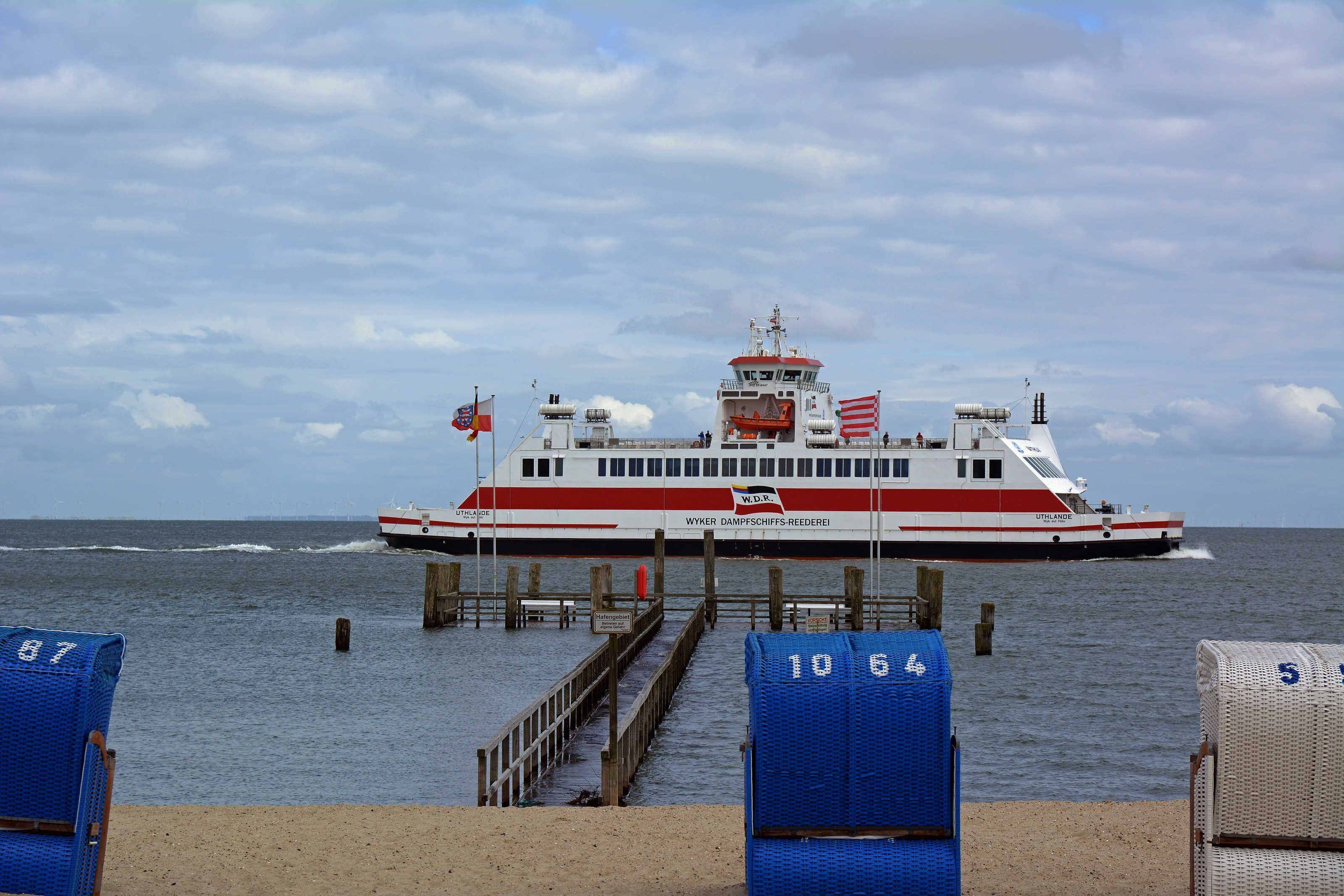 A ferry docked at a pier with a clear view of the water and a cloudy sky.