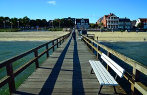 Un muelle de madera que conduce a una playa, con edificios al fondo.