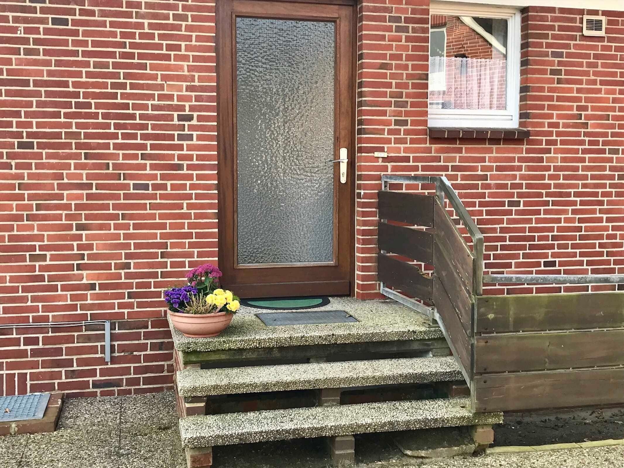 A brick building with a wooden door, a small window, and a set of concrete steps leading to a door.