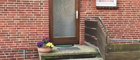 A brick building with a wooden door, a small window, and a set of concrete steps leading to a door.
