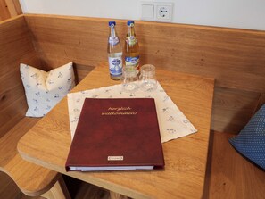 Una cadira de fusta amb un llibre vermell que diu 'Herzlich willkommen!' i dues botelles de cervesa damunt d'un taulell amb una estovada floral.