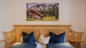 A double bed with a wooden headboard, two bedside tables, and a painting of a mountain lodge.