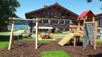 A playground with swings and climbing structures, a table with chairs, and a building with balconies and flower boxes in the background.