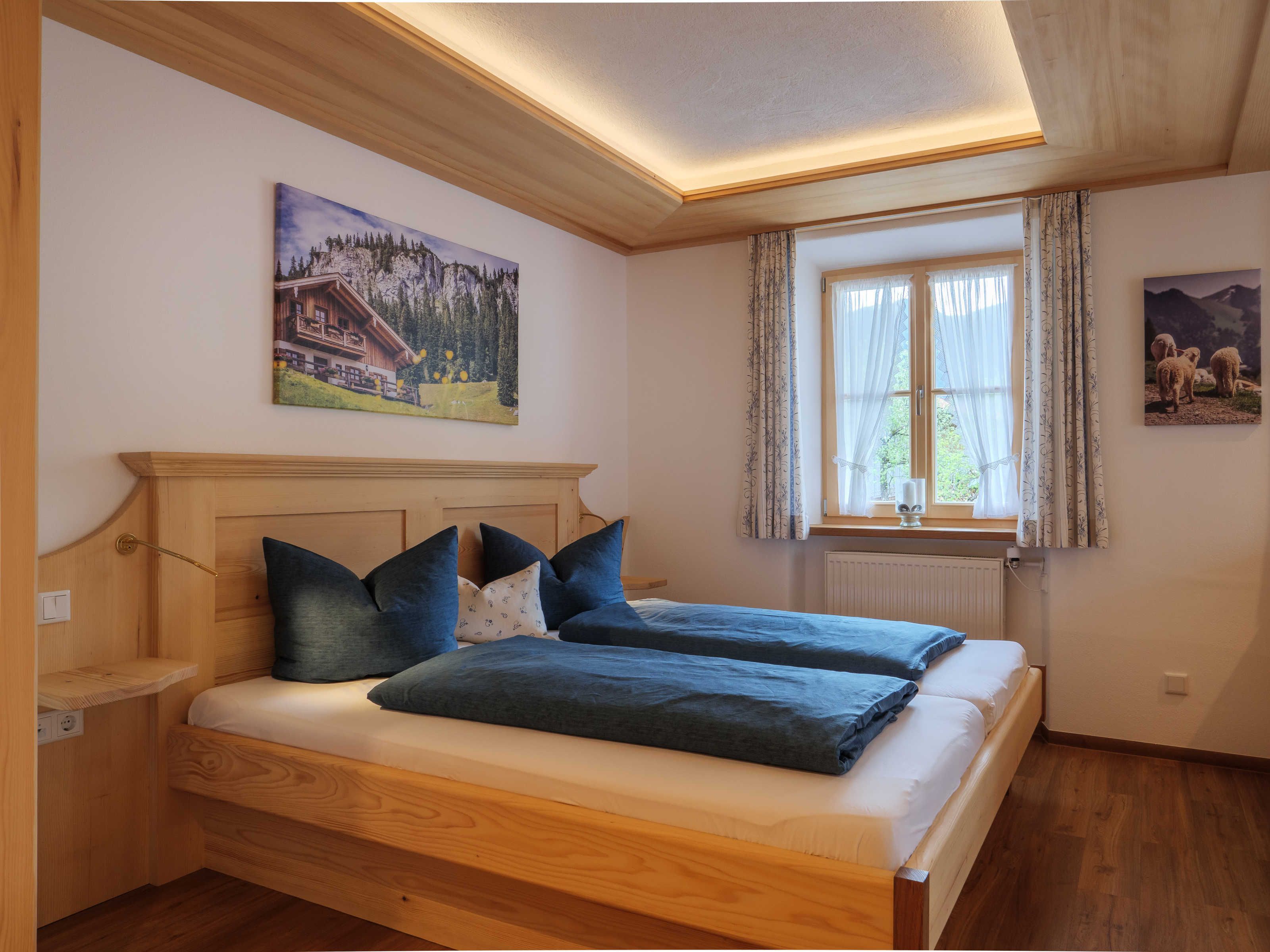 Un dormitorio con cama de madera, una ventana con cortinas, un cuadro en la pared y un radiador.