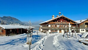 A traditional wooden building with a balcony, a snow-covered path, and a mountain in the background.