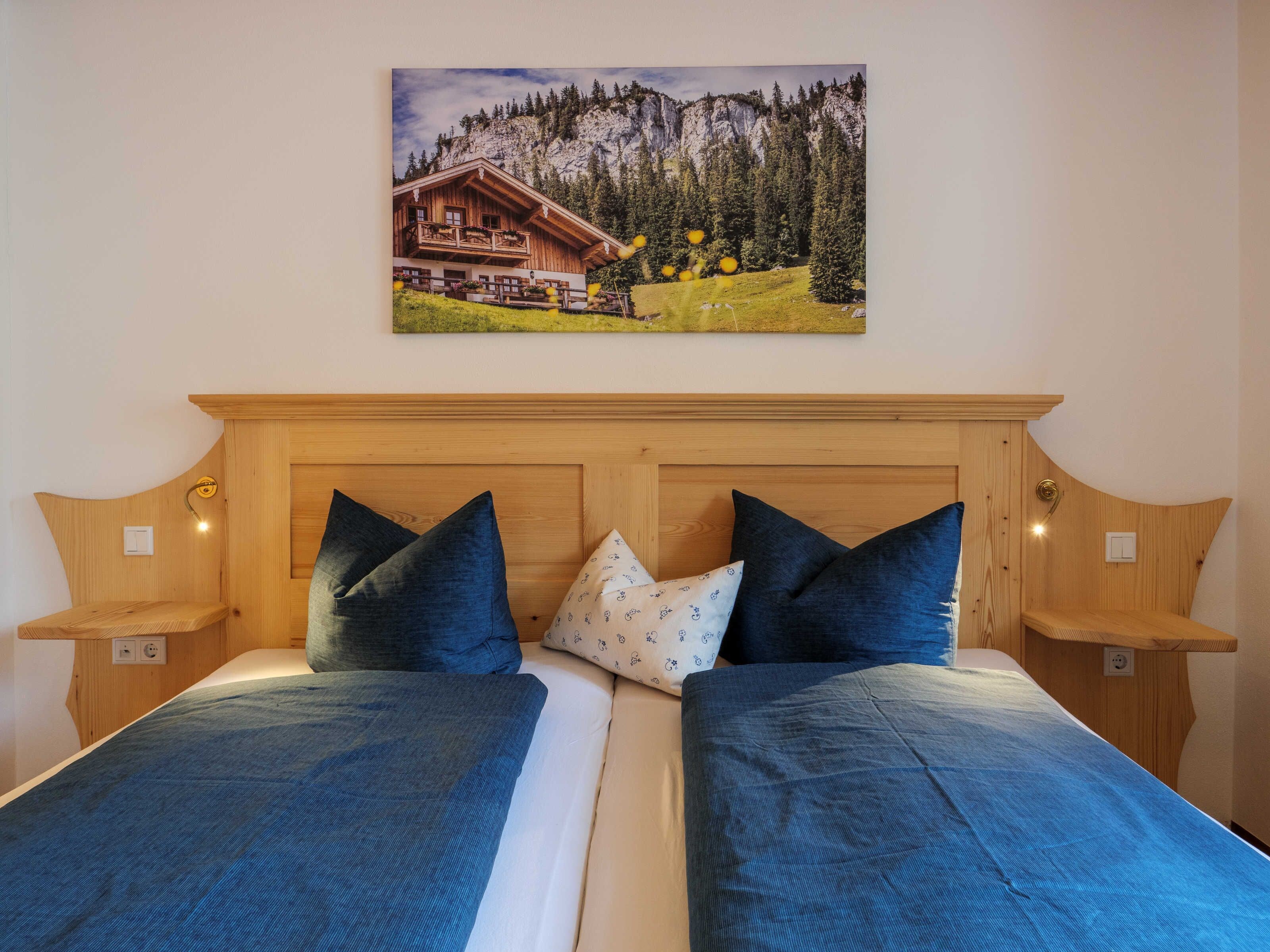 A double bed with a wooden headboard, two bedside tables, and a painting of a mountain lodge.