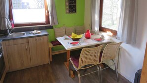 A small kitchen with a dining area, wooden cabinets, a sink, and a table set for two with chairs. - Vacation home 175 Mohikaner 40qm up to 5 persons with pet - Ferienhaus Mohikaner (Hollern-Twielenfleth)
