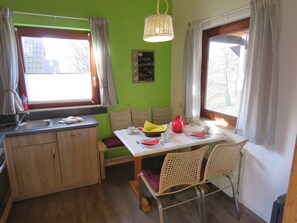 A small kitchen with a dining area, wooden cabinets, a sink, and a table set for two with chairs.