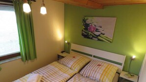 A double bed with striped bedding, a nightstand with a lamp, and a green wall with a floral painting. - Vacation home 175 Mohikaner 40qm up to 5 persons with pet - Ferienhaus Mohikaner (Hollern-Twielenfleth)