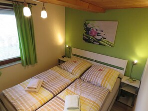 A double bed with striped bedding, a nightstand with a lamp, and a green wall with a floral painting.