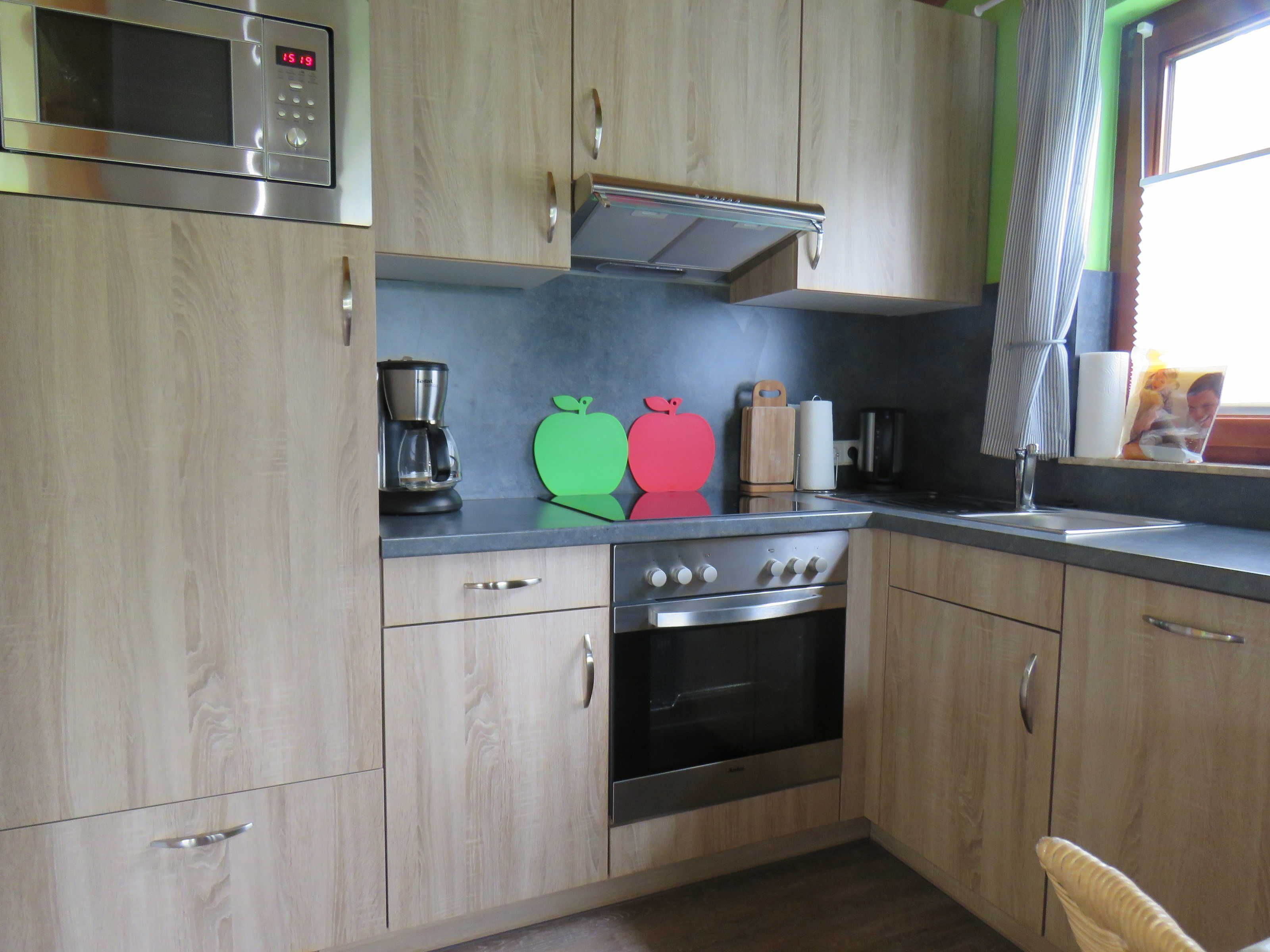 Una cocina con armarios de madera, microondas de acero inoxidable, cafetera y tostadora.