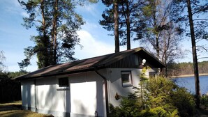Eine kleine Holzhütte mit geneigtem Dach, in der Nähe eines Gewässers, umgeben von Bäumen.