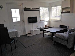A compact room with a single bed, a small table, a sofa, a television, and a window. - House 5 - Holiday home family Acker (Lychen)
