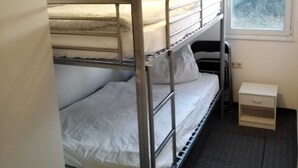 Ein Schlafraum mit Etagenbett, Fenster, kleinem Nachttisch und Deckenleuchte.