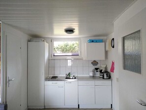 A compact kitchen with white cabinets, a window above the sink, and a clock on the wall.