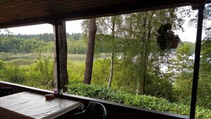 Ein Sitzbereich im Freien mit Tisch und Stühlen, mit Blick auf eine natürliche Landschaft mit Bäumen und einem Gewässer.