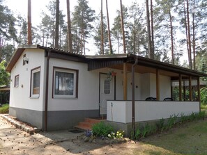 Un petit bâtiment d’un seul étage, doté d’un porche et entouré d’une forêt.