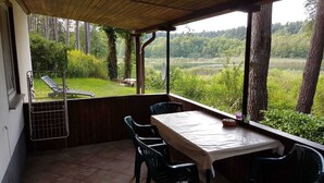 Eine überdachte Terrasse mit Tisch und Stühlen, mit Blick auf eine üppige Landschaft mit Bäumen und einem Gewässer.
