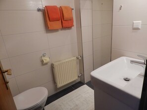 Un baño con inodoro, lavamanos, ducha y dos toallas colgadas en la pared.